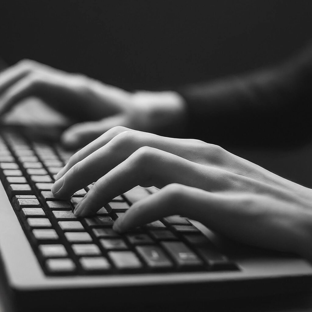 A persons hands on a keyboard. Black and white. Shows that the current section is about working for the RadicaLab Foundation, and that the work being done is office work. 